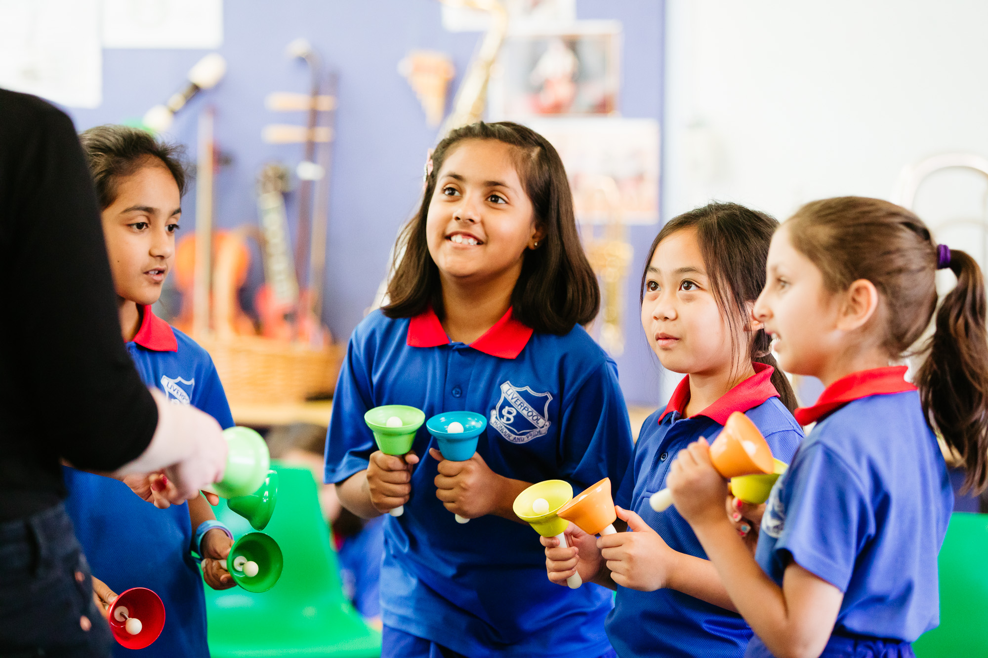 Primary school students holding bells while looking up at teacher