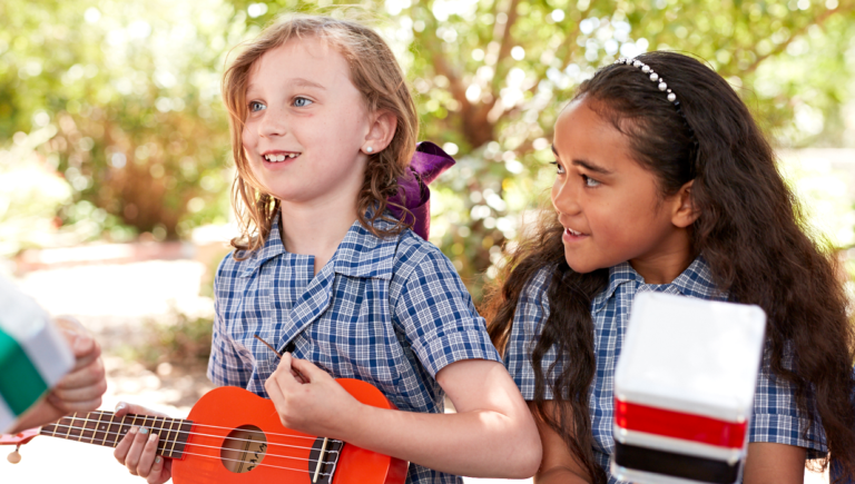 two primary school students engaged in Outdoor Music Classroom arts learning lesson on ukuleles